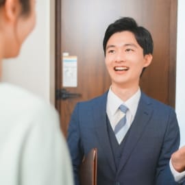 スーツ姿の営業マンが笑顔で訪問し、顧客と会話している様子