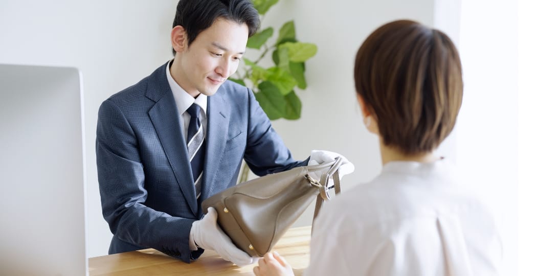 スーツ姿の鑑定士が白手袋を着用し、バッグを査定している様子
